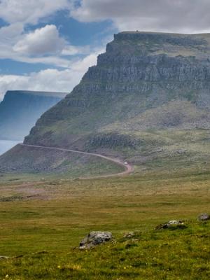 a road going through a grassy field with a mountain in the background .