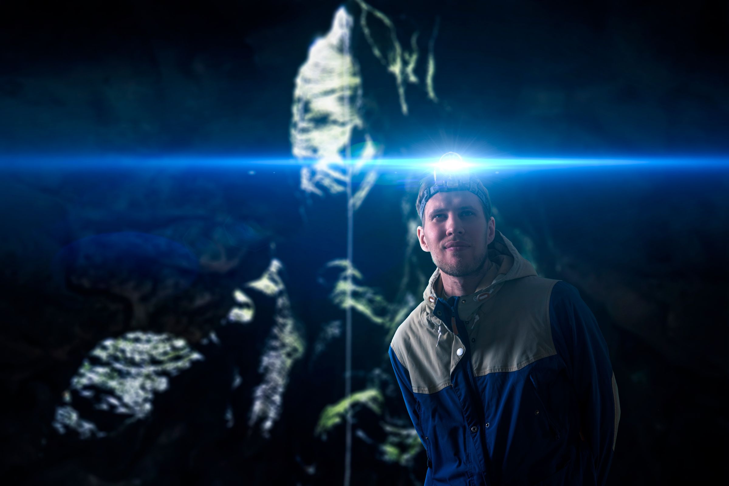 Un hombre con una lámpara en la cabeza emite una luz azul brillante y destello de lente en una cueva oscura.