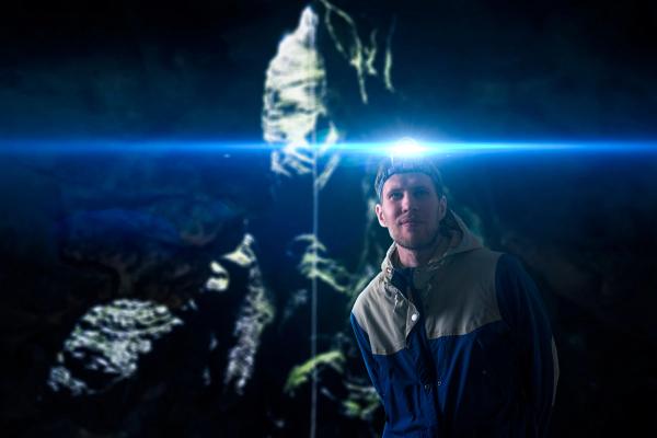 A man wearing a headlamp casts a bright blue light and lens flare in a dark cave.