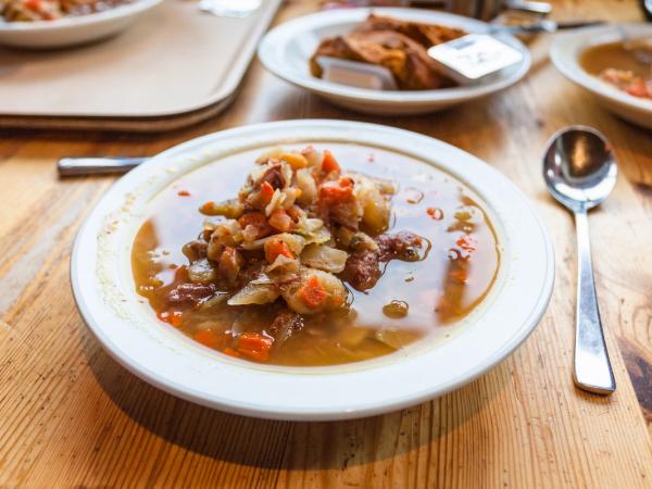 A bowl of chunky vegetable soup with a spoon on a wooden table.