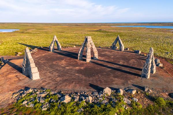 The Arctic Henge, a circular formation of large stone arches and pillars, in a vast green landscape with distant lakes.