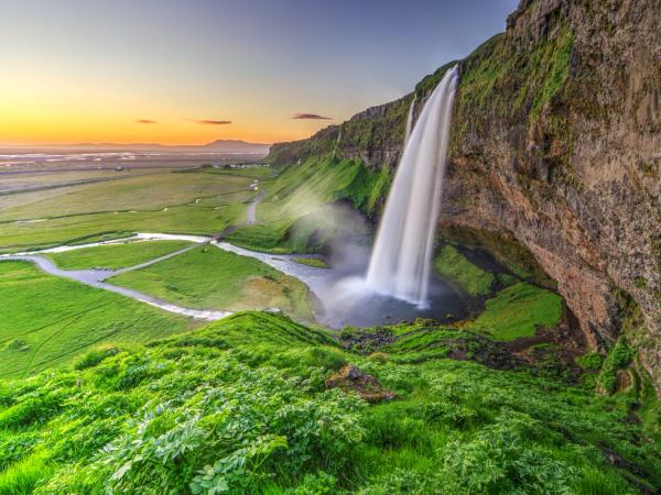 a waterfall in the middle of a green field with a sunset in the background .