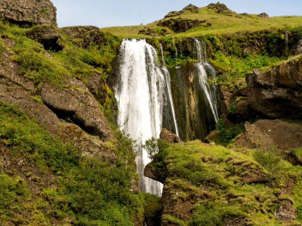 a waterfall is surrounded by rocks and grass on a hillside .