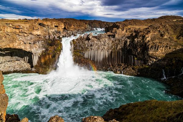 una cascada en medio de un cañón con un arcoíris en el agua.
