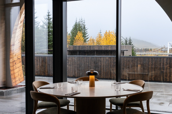 A modern restaurant interior with a round table set for four and a glowing lamp, looking out at autumn trees.