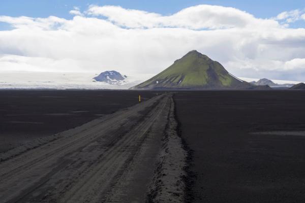 F210 – Fjallabaksleið Syðri F-road in Iceland view on dirt mountain road F210 in black lava sand desert at Nature reserve Fjallabak in Iceland with green Maelifell mountain and myrdalsjokull glacier, blue sky white clouds