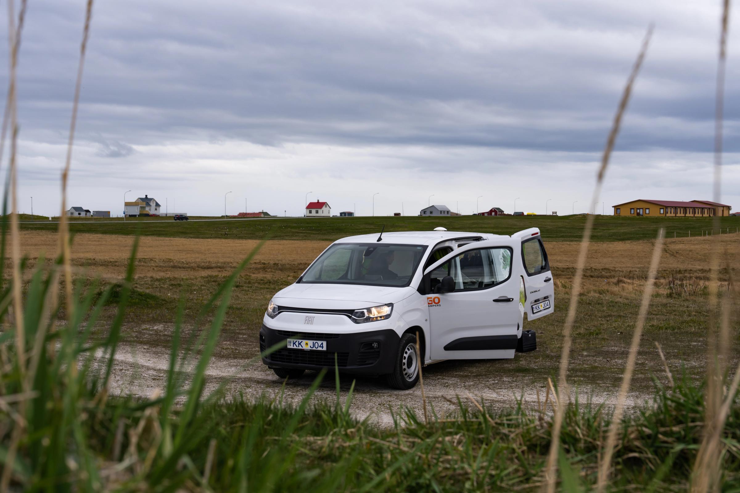 Una autocaravana compacta para 2 personas en un camino de grava, con las puertas abiertas, alquiler de autocaravanas en Islandia