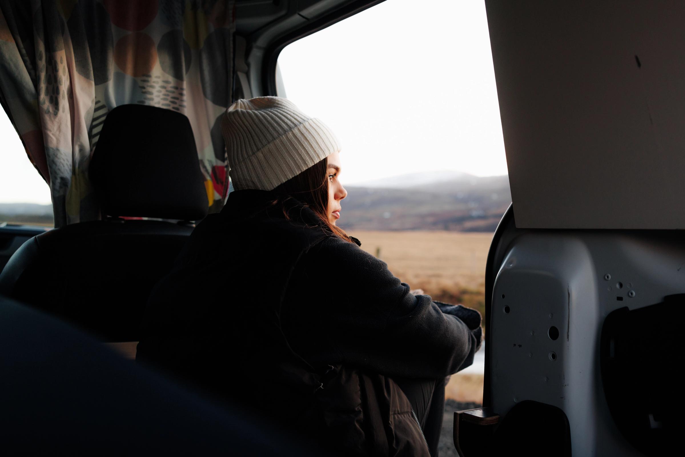 Eine Person sitzt drinnen an der offenen Schiebetür und blickt hinaus auf eine weite Landschaft.