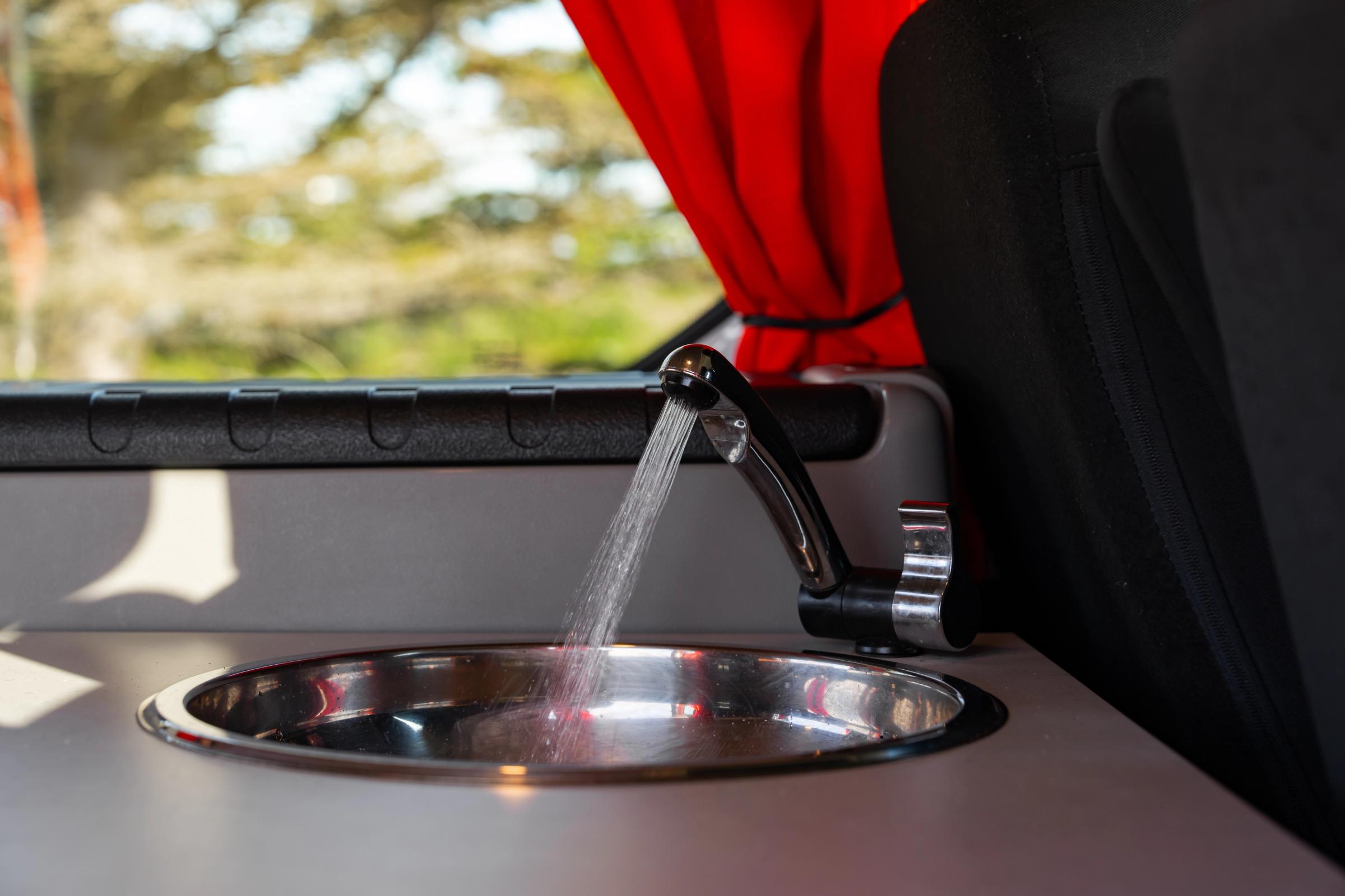 Close-up of water running from a tap into a round stainless steel sink