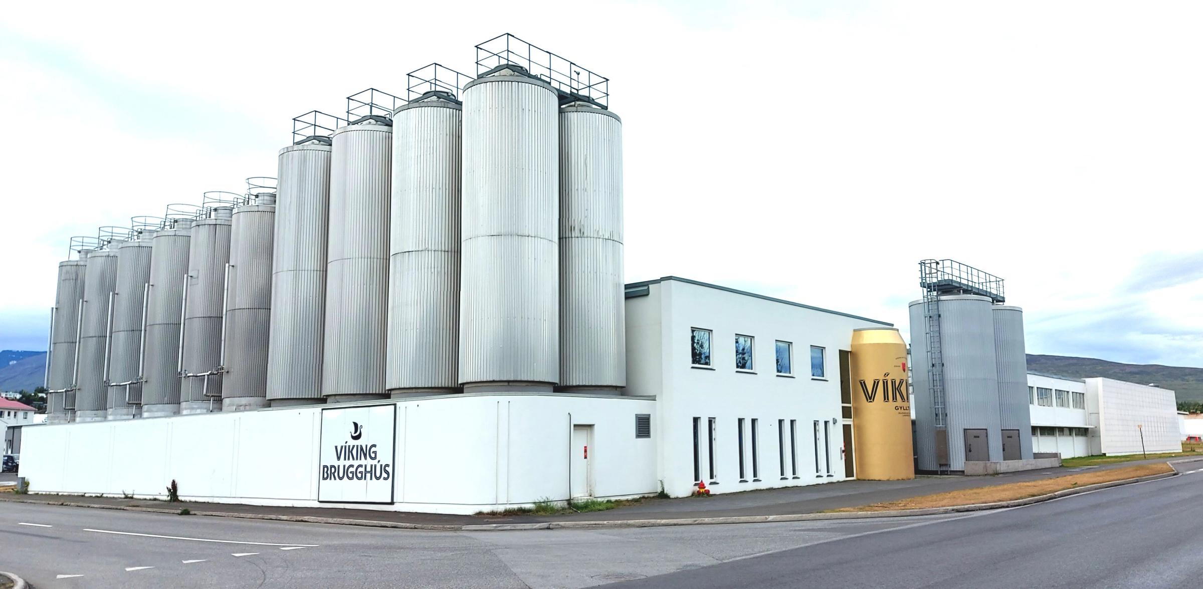Exterior view of the Viking Brugghús brewery with numerous silver silos and a giant golden Viking beer can replica.