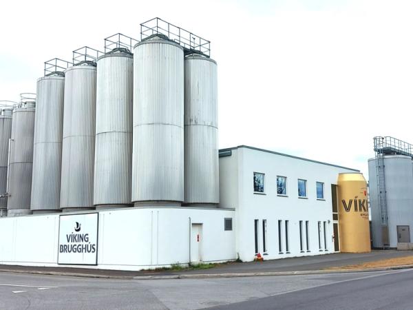 Exterior view of the Viking Brugghús brewery with numerous silver silos and a giant golden Viking beer can replica.