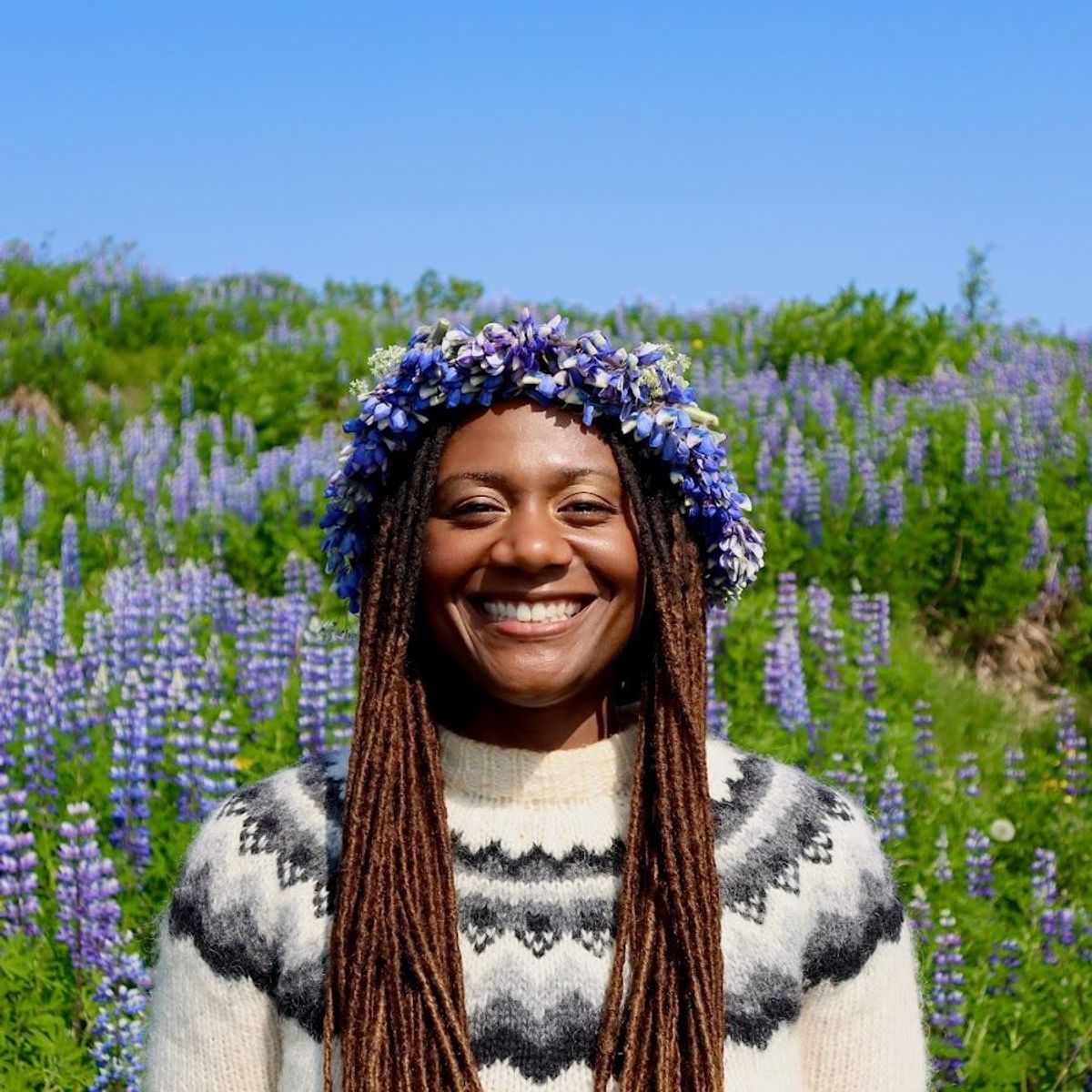 Une femme portant une couronne de fleurs sourit dans un champ de fleurs violettes.