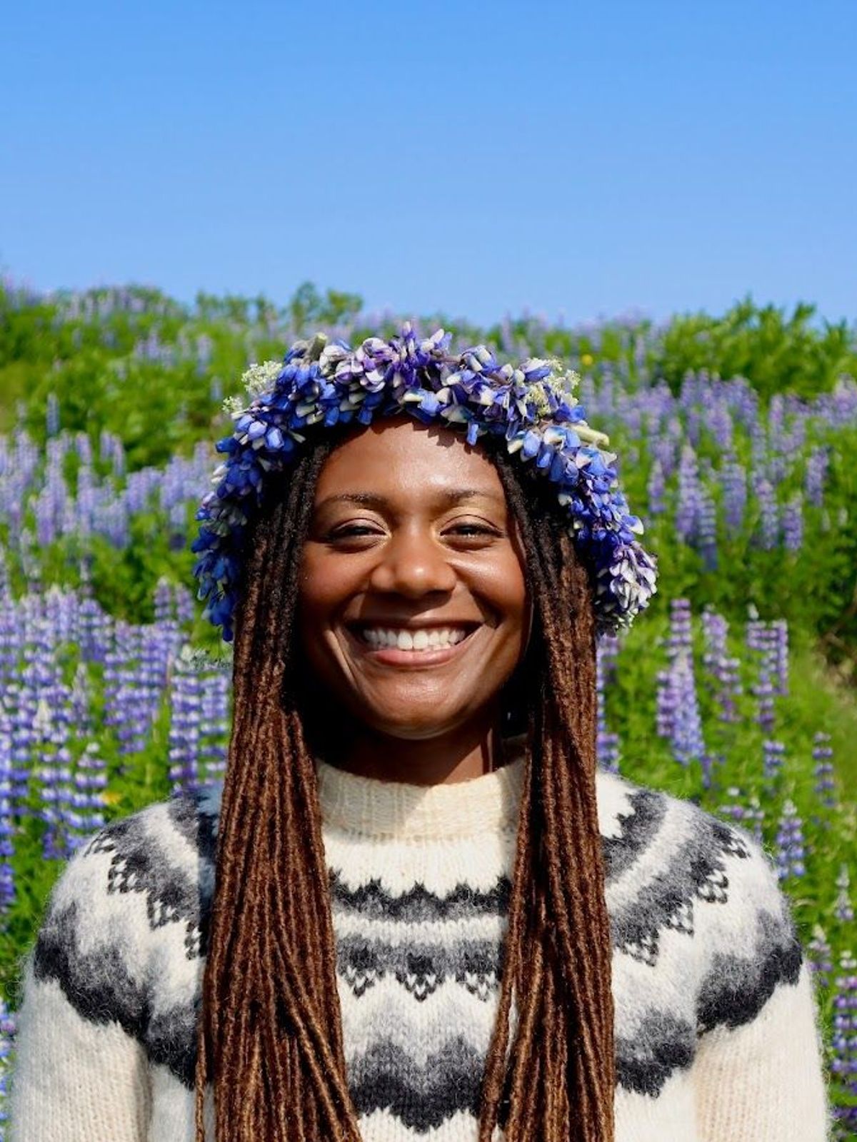 Une femme portant une couronne de fleurs sourit dans un champ de fleurs violettes.