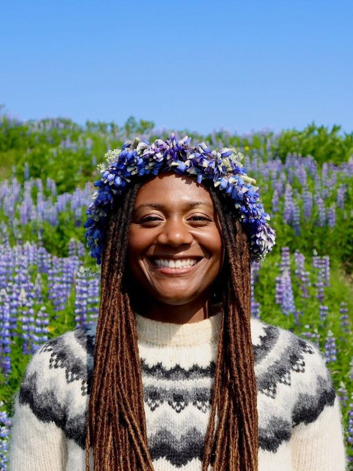 a woman wearing a flower crown is smiling in a field of purple flowers .