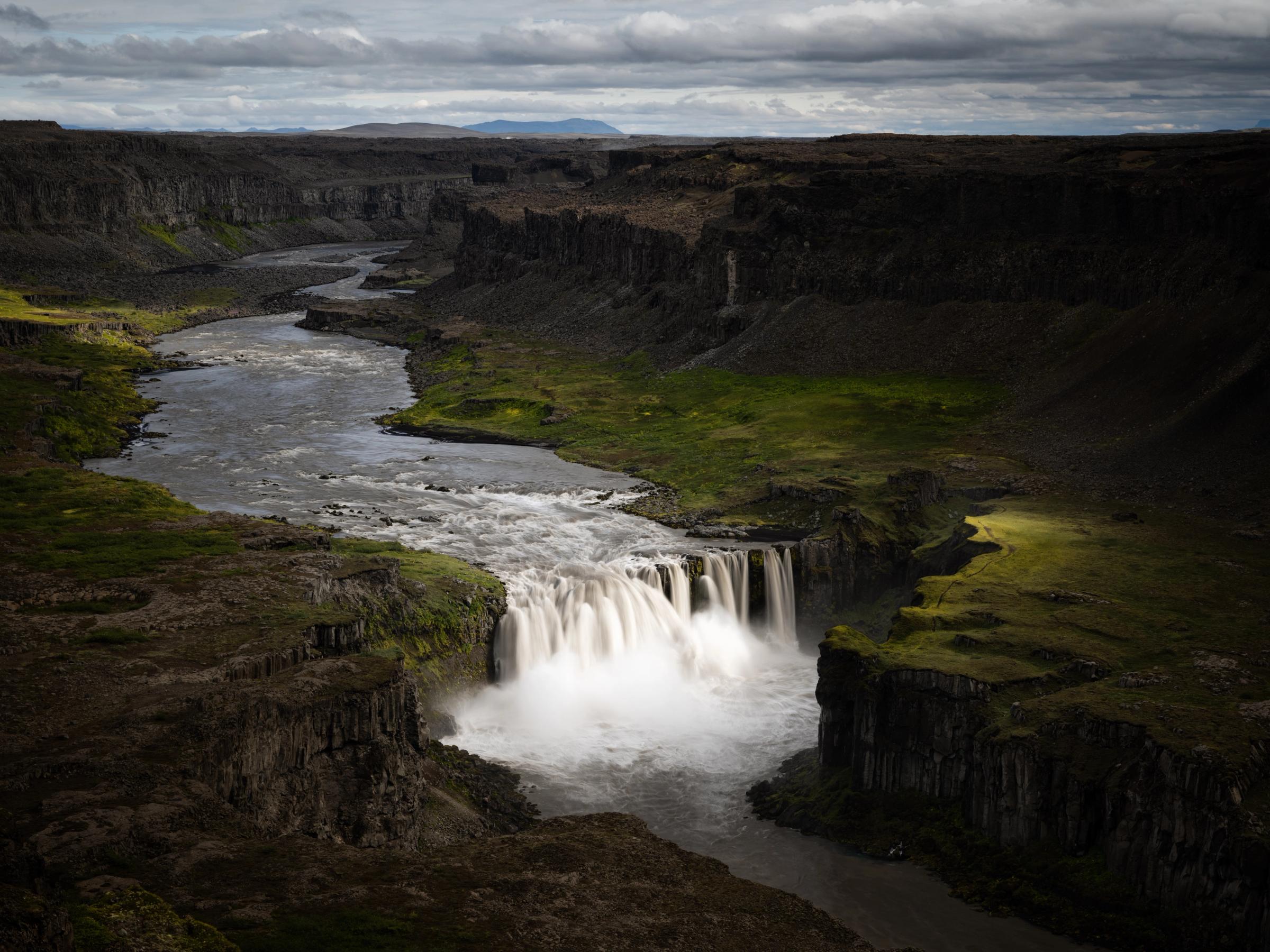 a waterfall in the middle of a canyon next to a river .