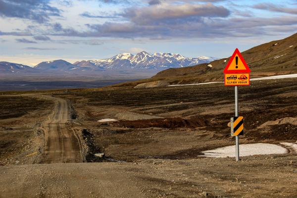 a dirt road with a sign on the side of it and mountains in the background at kjölur in iceland.
