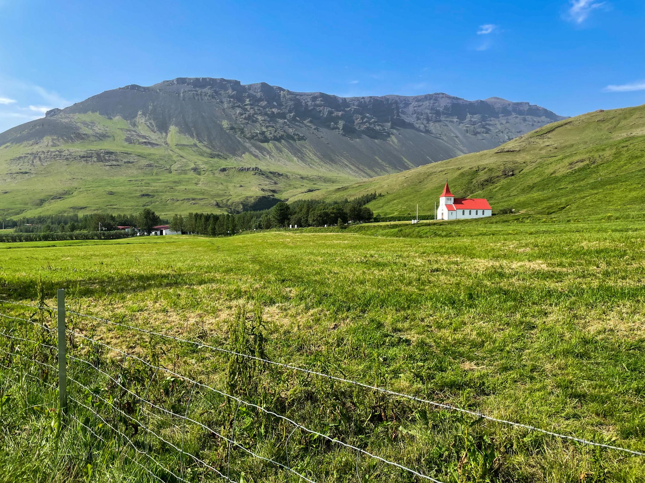 White and red church in the middle of a green valley