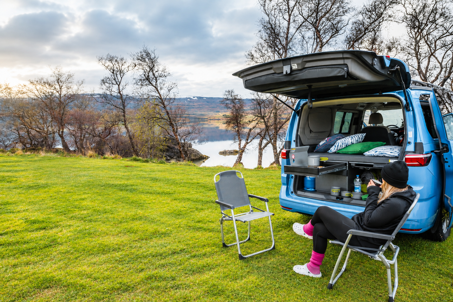 Person in a camping chair behind the camper with tailgate open and kitchen out, Iceland campervan