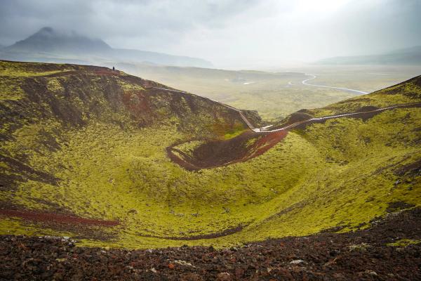 a large crater in the middle of a grassy hillside with a mountain in the background .