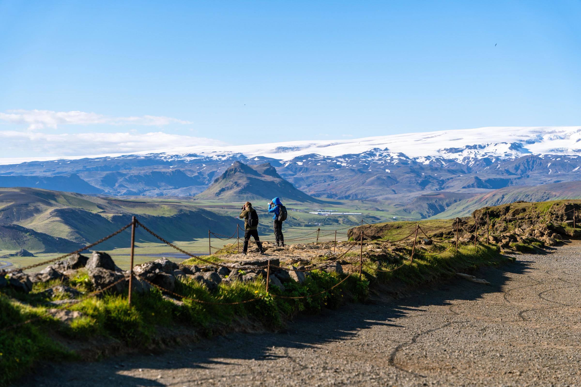 dos personas haciendo senderismo y admirando las vistas de un valle con una montaña nevada al fondo