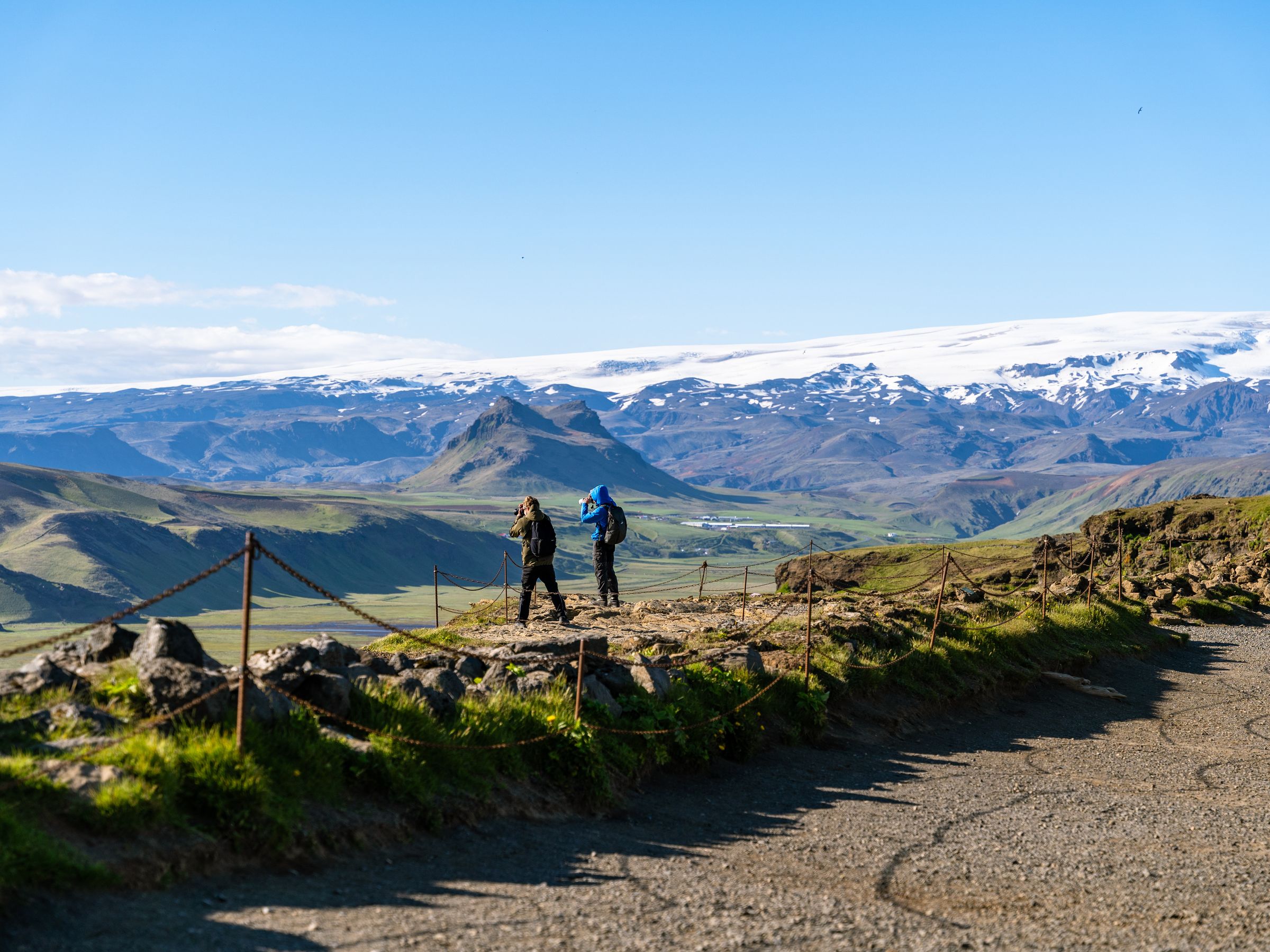 dos personas haciendo senderismo y admirando las vistas de un valle con una montaña nevada al fondo