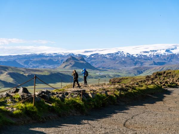 two people hiking and admiring the views of a valley with a mountain on the background