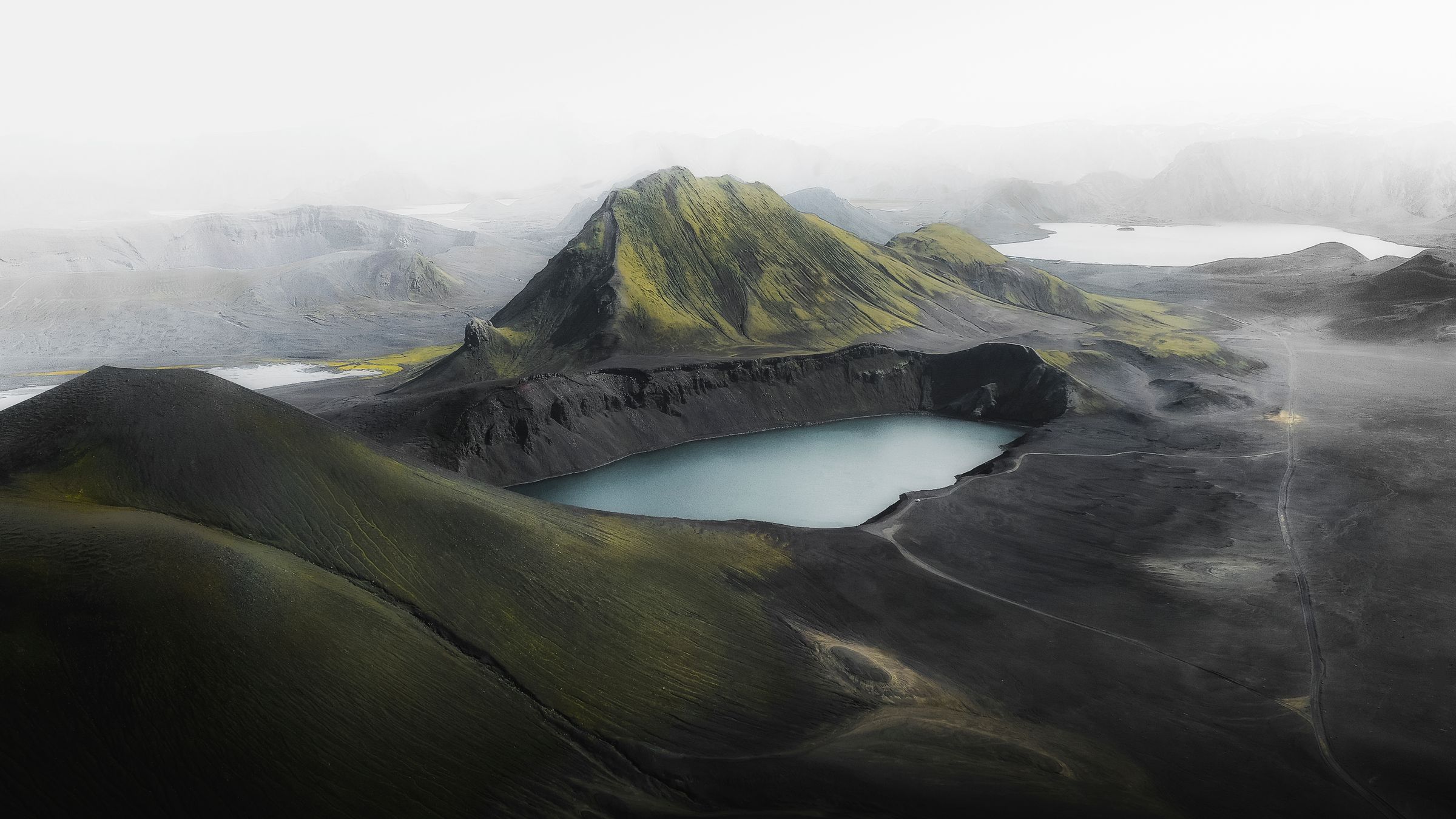 a crater with a lake in a volcanic landscape surrounded by fog