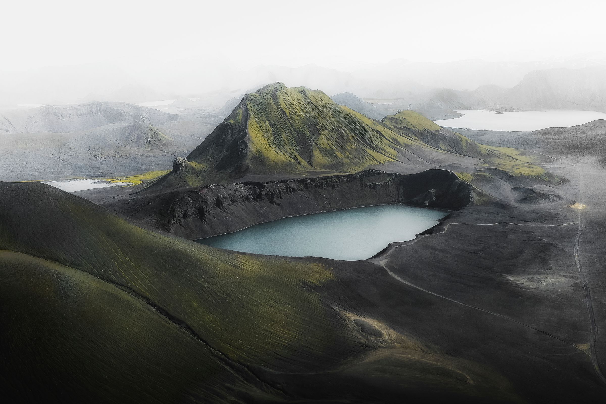 a crater with a lake in a volcanic landscape surrounded by fog