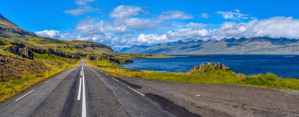 a road going through a valley with mountains and a lake in the background .