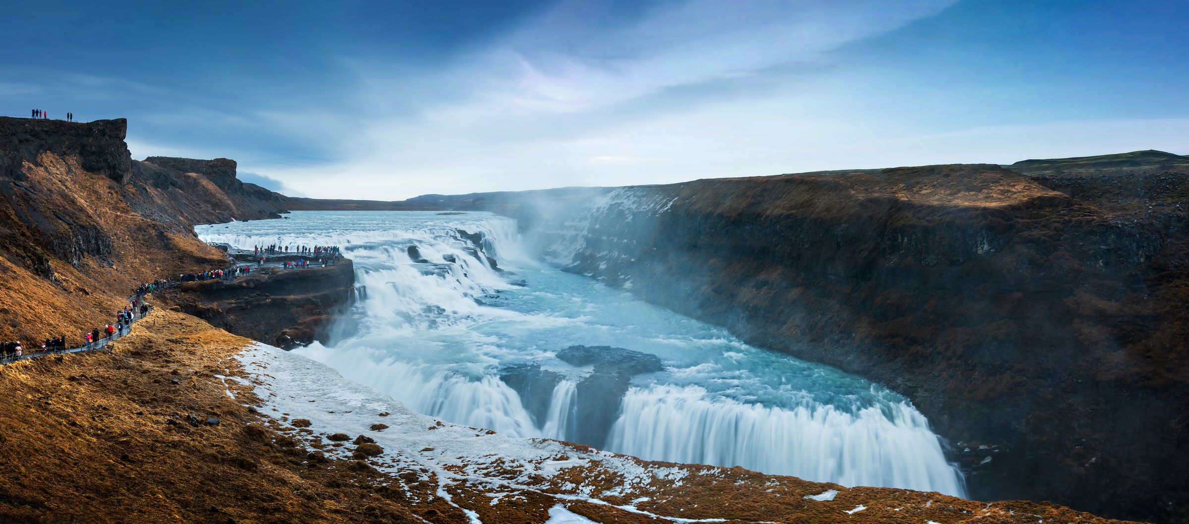 a group of people are standing on a cliff overlooking a Gullfoss waterfall in iceland .