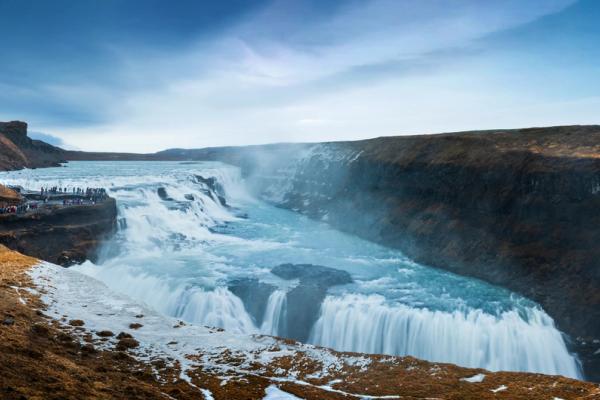 a group of people are standing on a cliff overlooking a Gullfoss waterfall in iceland .