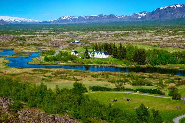 an aerial view of a lush green field with a river and mountains in the background .