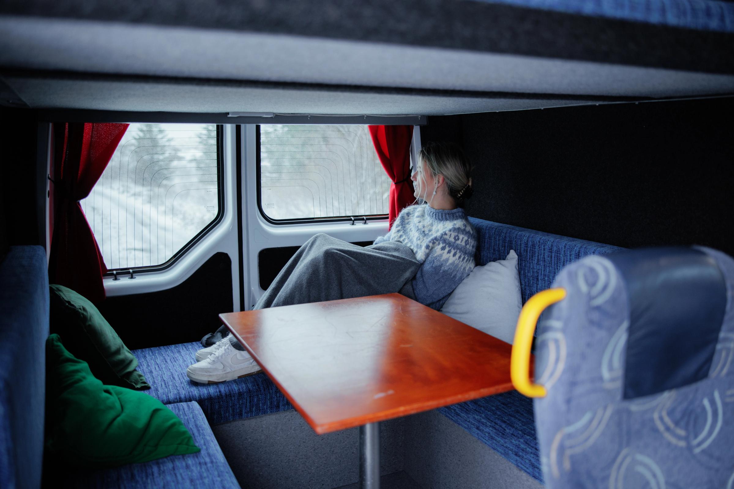 Frau, die sich auf der gepolsterten Sitzbank am Tisch in einem großen Camper für fünf Personen ausruht