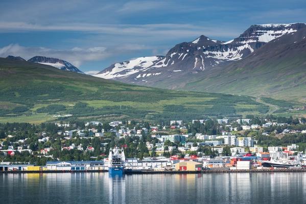 A town on a bay with a harbor, surrounded by green hills and snow-capped mountains.