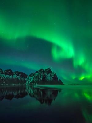 the aurora borealis is reflected in the water over the mountains .
