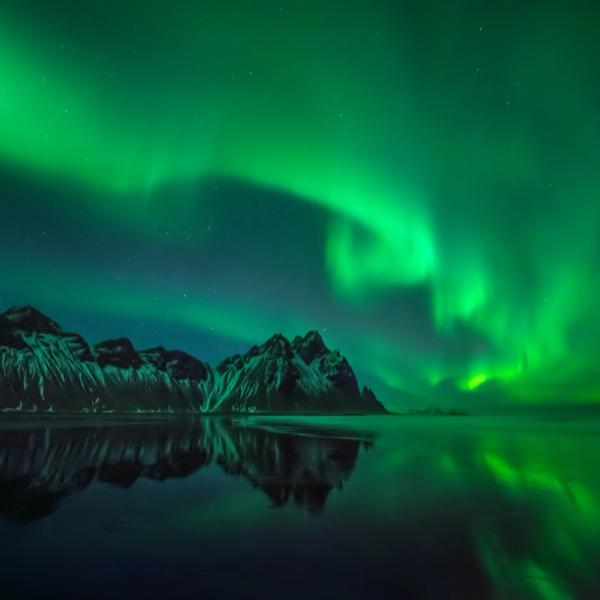 La aurora boreal sobre unas montañas se refleja en el agua.