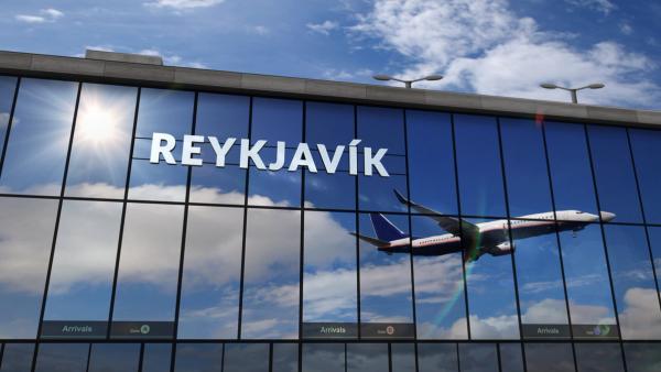 Glass airport terminal building with "REYKJAVÍK" sign, reflecting a bright sky and an airplane.
