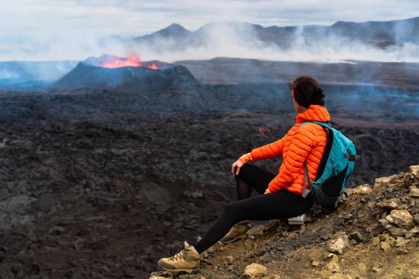 a woman is sitting on top of a mountain looking at a volcano.
