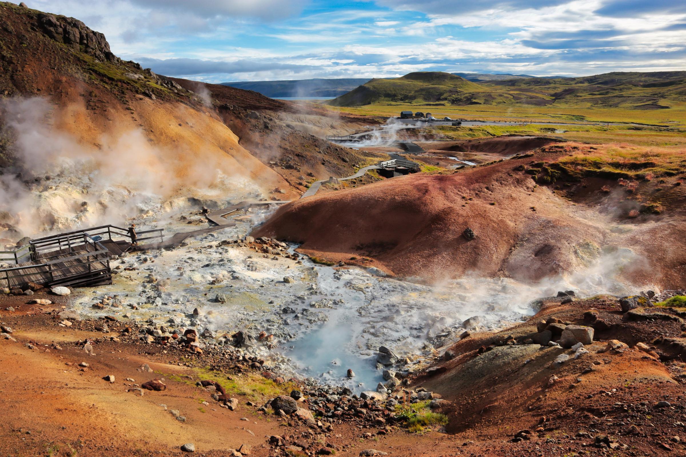Colorful, steaming geothermal landscape with mineral-rich ground and visitor boardwalks.