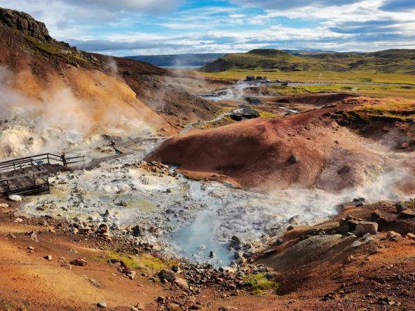 Colorful, steaming geothermal landscape with mineral-rich ground and visitor boardwalks.