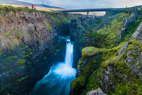 a waterfall in the middle of a canyon with a bridge in the background .