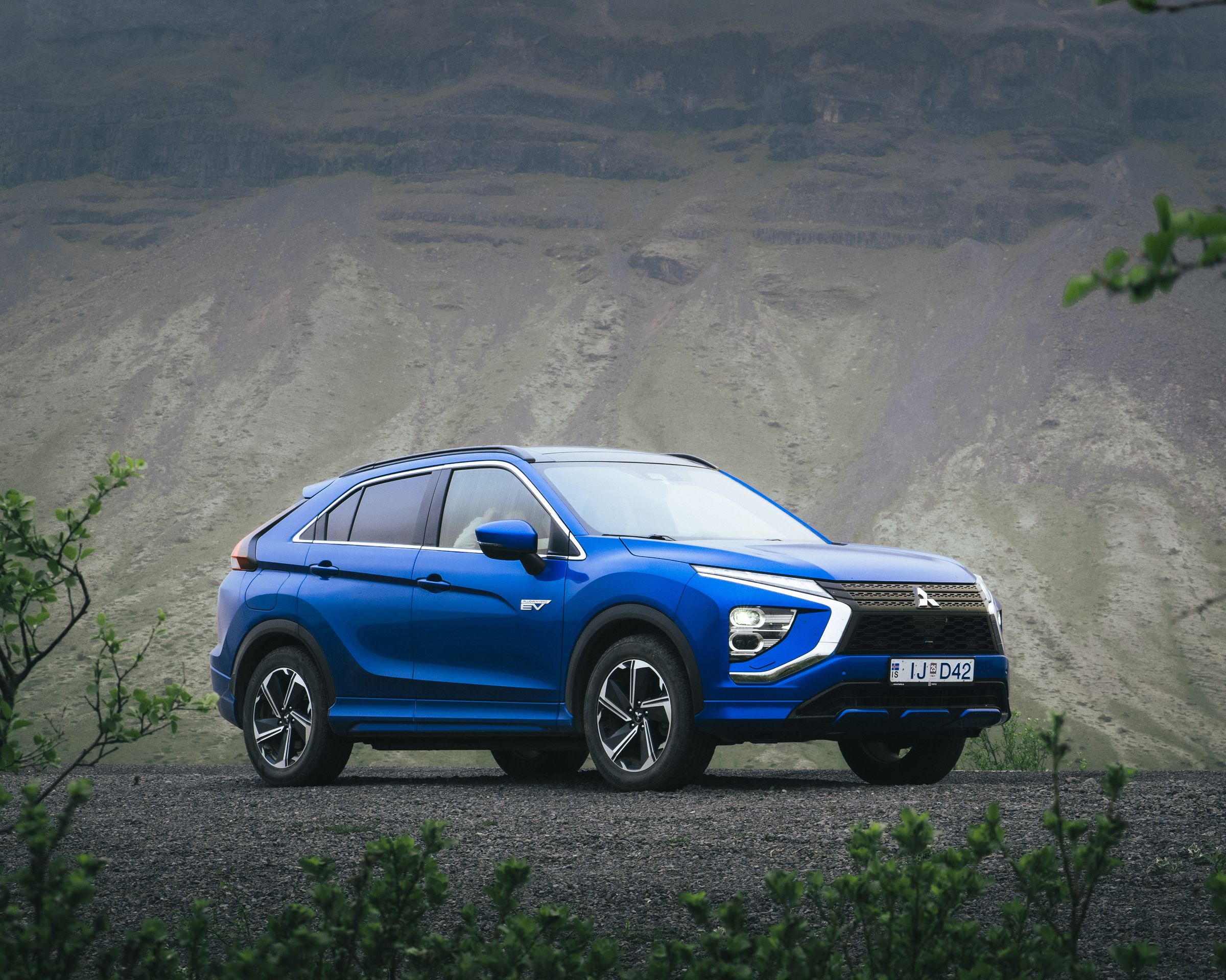 Mitsubishi Eclipse Cross aparcado sobre grava, rodeado de vegetación y con una ladera rocosa de montaña al fondo