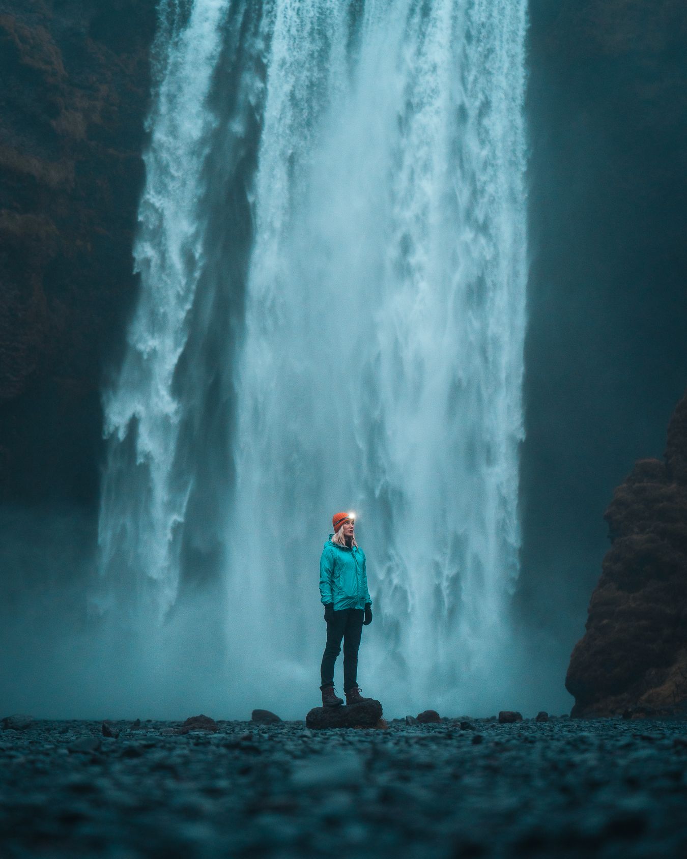 Mujer con un gorro rojo y una chaqueta impermeable azul en frente de una cascada