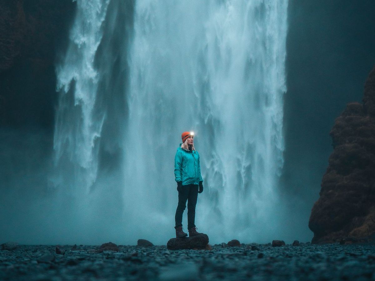 Mujer con un gorro rojo y una chaqueta impermeable azul en frente de una cascada