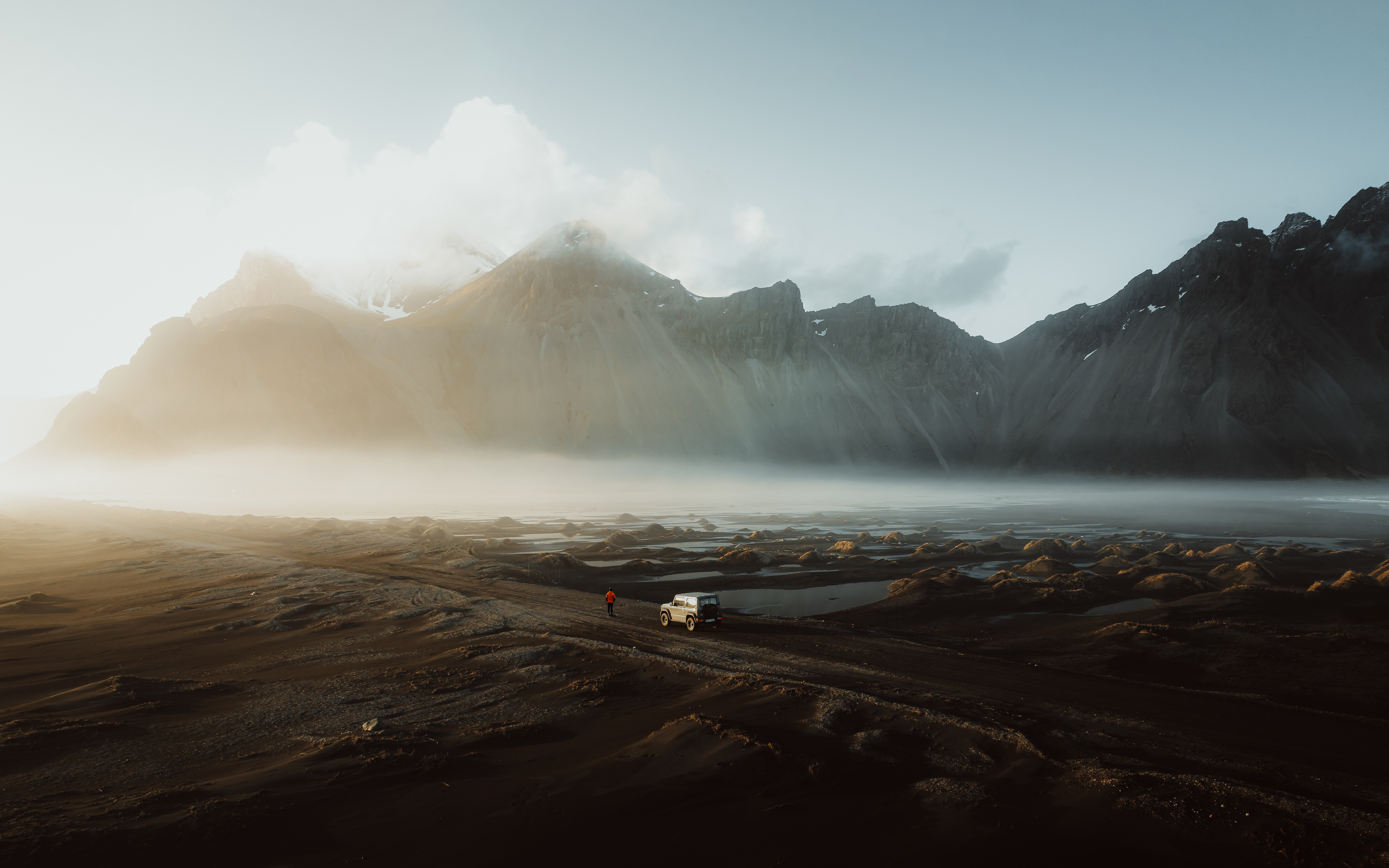 a car is parked on a dirt road with mountains in the background