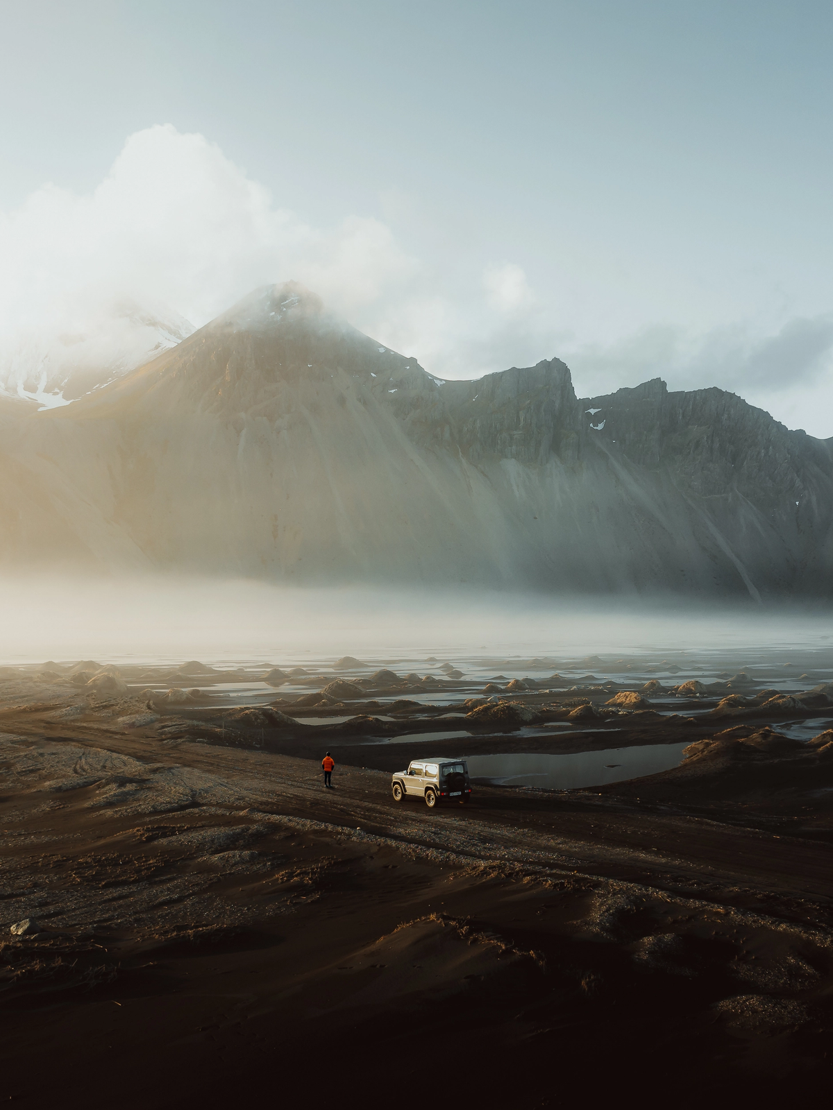 a car is parked on a dirt road with mountains in the background