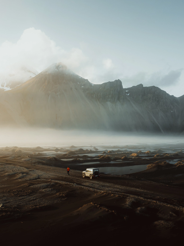 a car is parked on a dirt road with mountains in the background