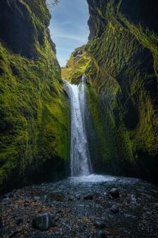 une cascade au milieu d'un canyon entouré de mousse verte à Nauthúsagil en Islande.