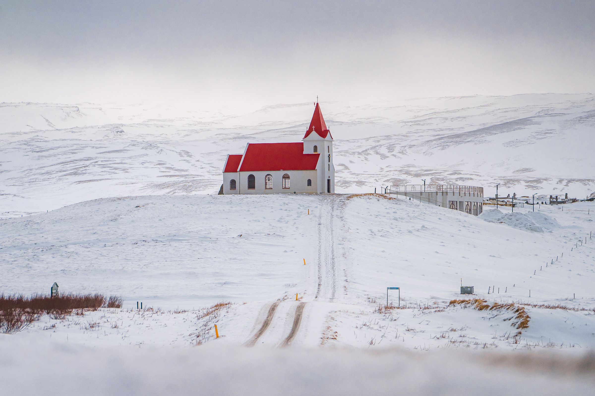 a small white church with a red roof is sitting on top of a snow covered hill .