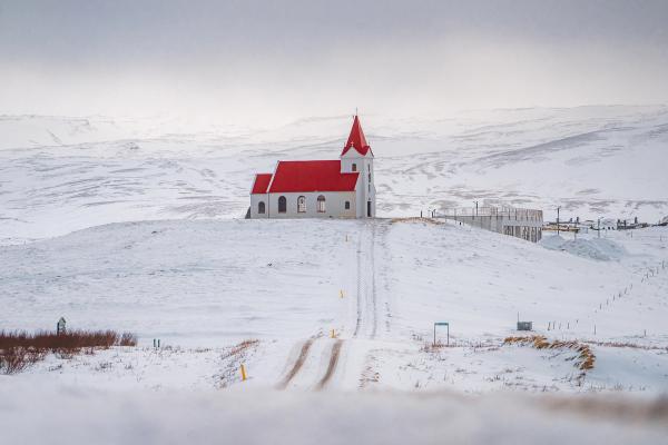 a small white church with a red roof is sitting on top of a snow covered hill .